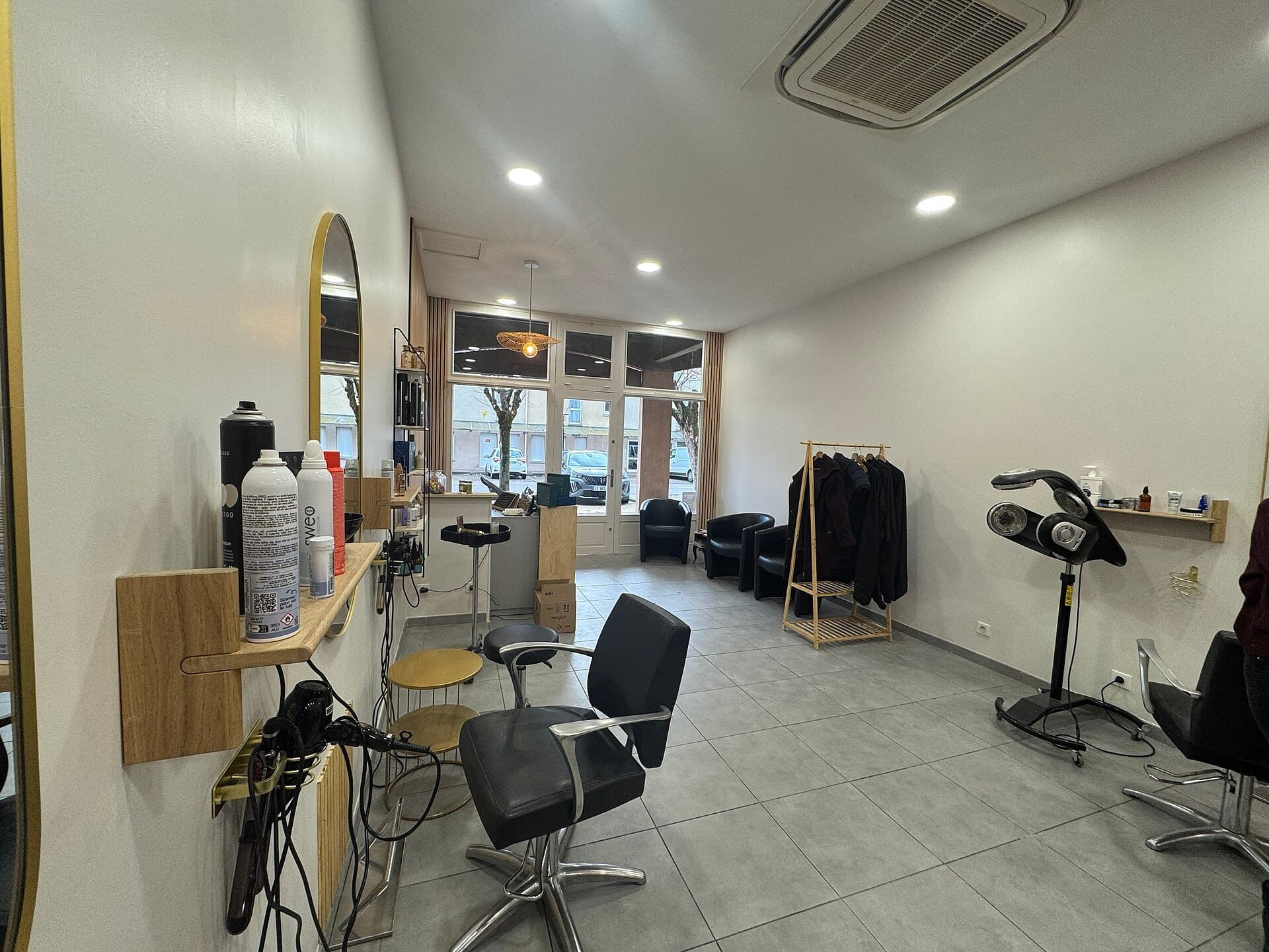 Single-station salon interior with a styling chair, brass-framed mirror, and product shelf